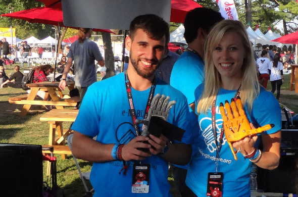 Maker Faire New York 2014: e-Nable Booth featuring a young adult male at left and a young adult female at right, both of whom are holding prosthetic arms in their hands.