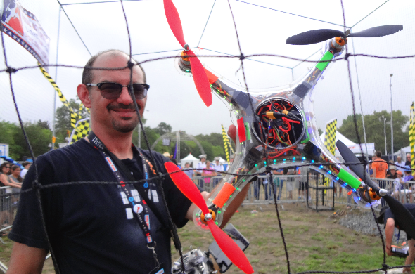 Maker Faire New York 2014: War of Drones photo showing an adult male gentleman holding a large drone in one hand. He is standing in the Game of Drones cage arena.